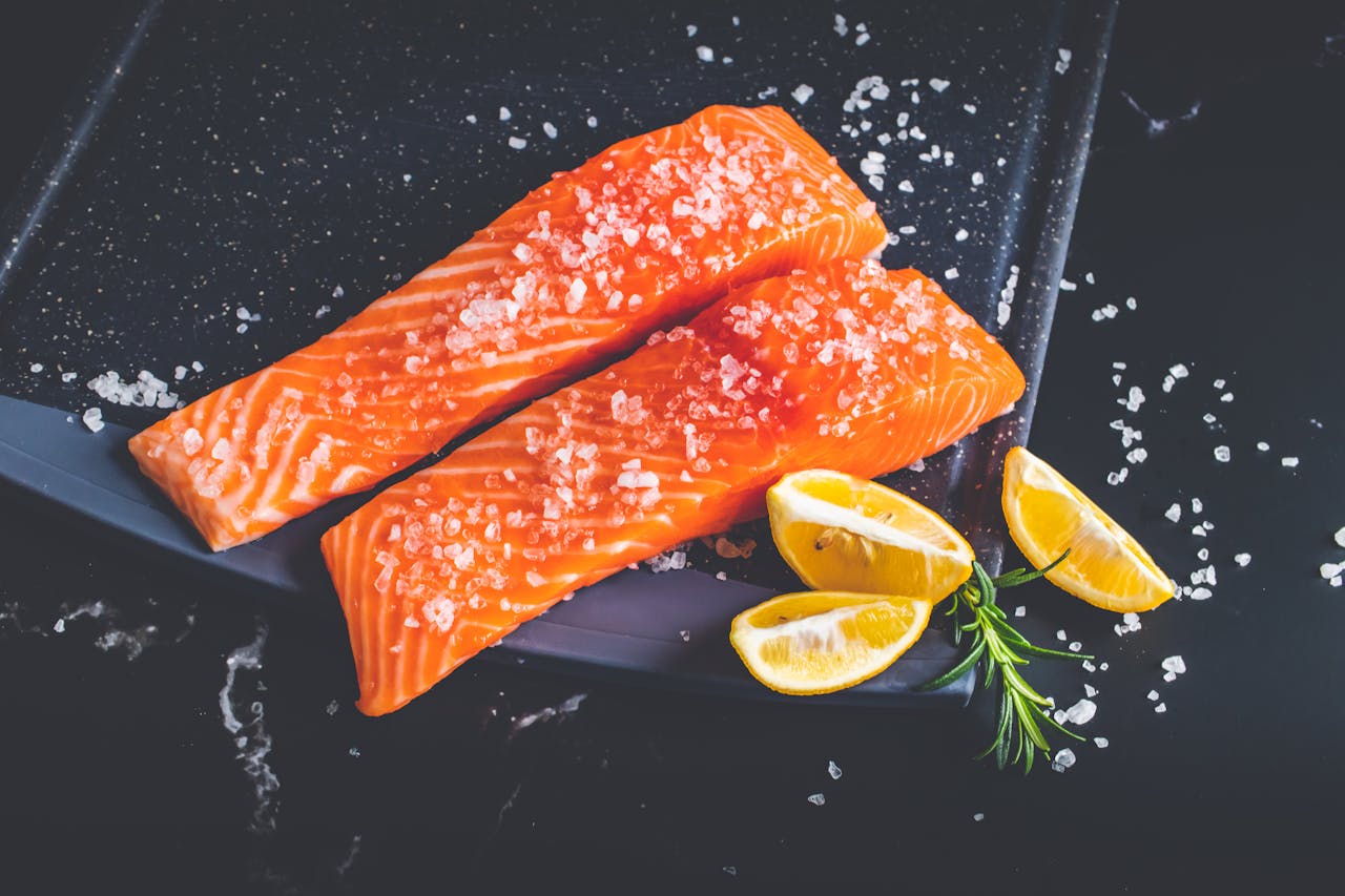 Close-up of raw salmon fillets garnished with salt, lemon wedges, and rosemary on a baking tray.